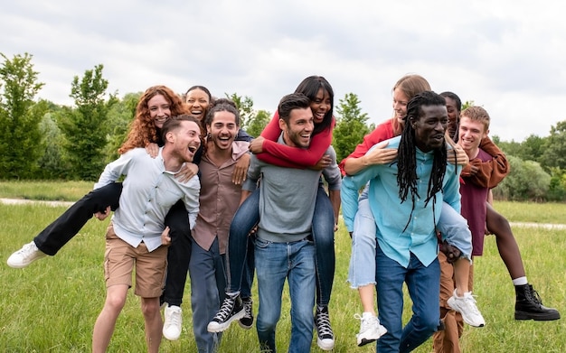 Group of best friends and young couples having fun at the park doing piggyback races international group of young happy students at public park playing