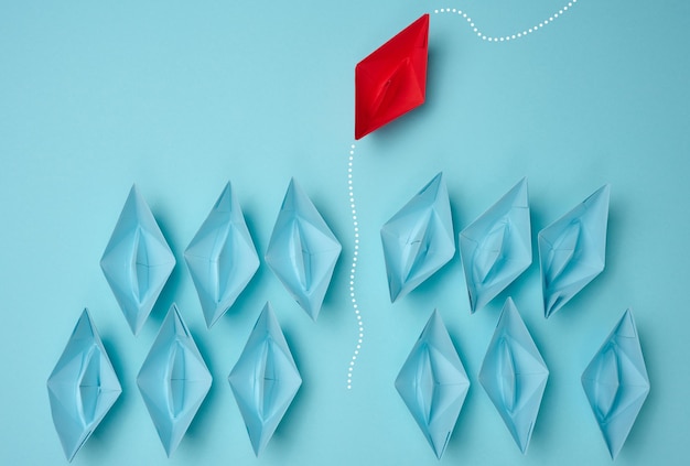 A group of blue paper boats heading in one direction and one
red one heading in the opposite direction. the concept of
individuality, uniqueness and talent of the employee. get away from
the influence