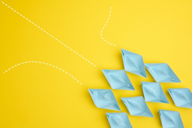 Photo group of blue paper boats with different paths on yellow background, path choice concept. teamwork