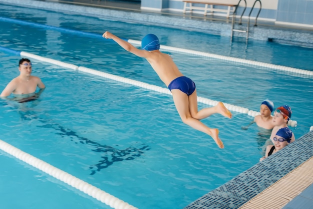 男の子と女の子のグループがトレーニングを行い、インストラクターと一緒にプールで泳ぐことを学びます。子供のスポーツの発展。