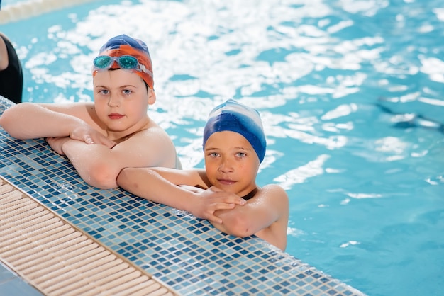 Un gruppo di ragazzi e ragazze si allena e impara a nuotare in piscina con un istruttore. sviluppo di sport per bambini.