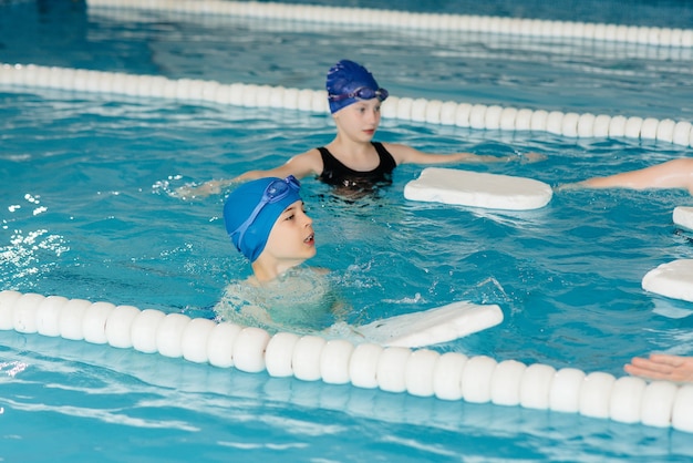 A group of boys and girls train and learn to swim in the pool with an instructor. Development of children's sports.