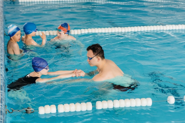 Группа мальчиков и девочек тренируется и учится плаванию в бассейне с инструктором. Развитие детского спорта.