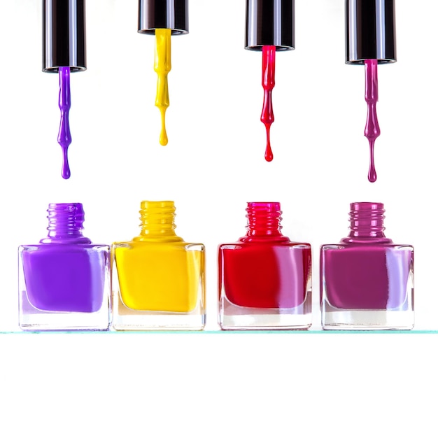Группа ярких красочных бутылочек лака для ногтей разных цветов на белом фоне с капельками и кистью. Абстрактный маникюр и макияж фон