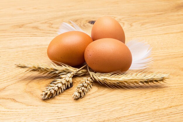 A group of brown eggs with feather and corn ears on wooden background.