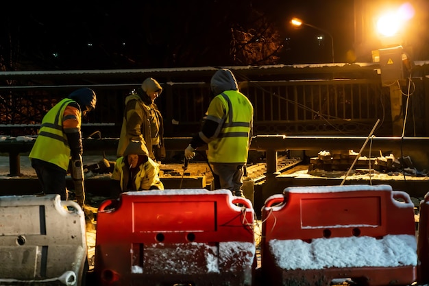 A group of builders repairs a bridge across the river at night\
under the light of lanterns in difficult winter conditions road\
repairs in winter during severe frosts