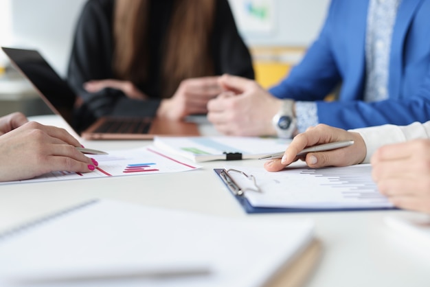 Group of business people are sitting at table with laptop and documents with charts closeup