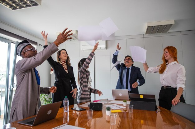 Группа деловых людей празднует достижение в бизнесе, подбрасывая бумаги в воздух