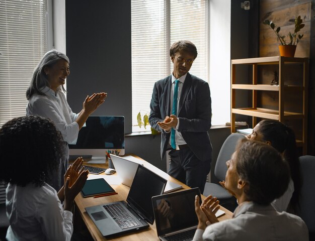 Group of business people congratulates applauds to a supervisor speech looking at computer with blac...