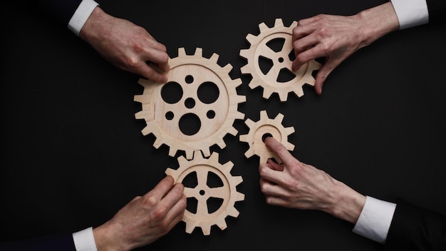 Group of business people connecting wooden cogwheels together on black background