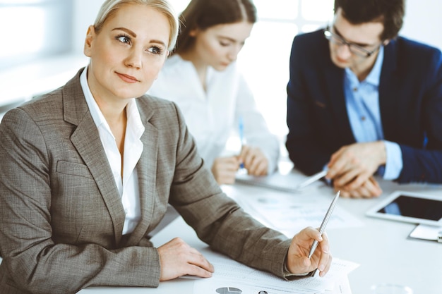 Group of business people discussing questions at meeting in modern office. Headshot of business woman at negotiation. Teamwork, partnership and business concept.