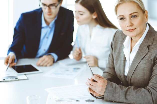 Group of business people discussing questions at meeting in modern office. Headshot of business woman at negotiation. Teamwork, partnership and business concept.