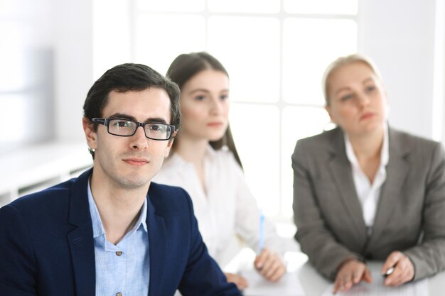 Group of business people discussing questions at meeting in modern office. Headshot of businessman at negotiation. Teamwork, partnership and business concept.