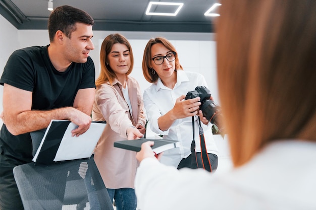 Group of business people in formal clothes indoors in the office looking at photos on the camera