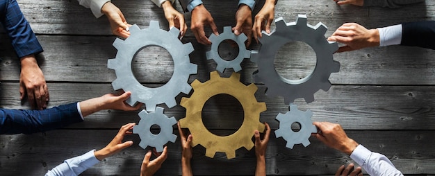 Photo group of business people joining together silver and golden colored gears on table at workplace top view