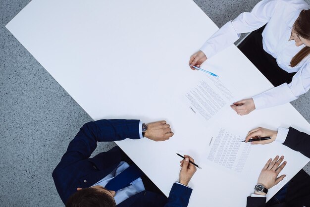 Group of business people and lawyer discussing contract papers sitting at the table, view from above. Businessman is signing document after agreement done.