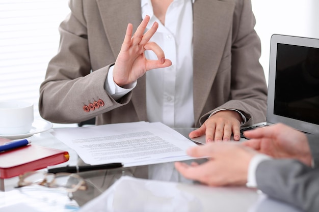 Group of business people or lawyers at meeting  discussing contract papers. Woman showing ok sign