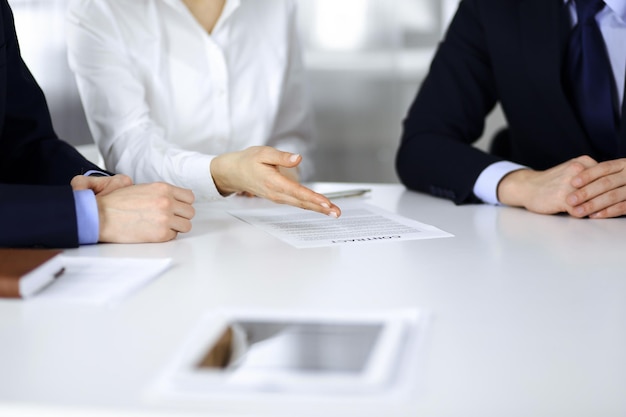 Group of business people, men and a woman, discuss details of a contract at meeting in a modern office. Discussion at negotiation or workplace. Teamwork, partnership and business concept.