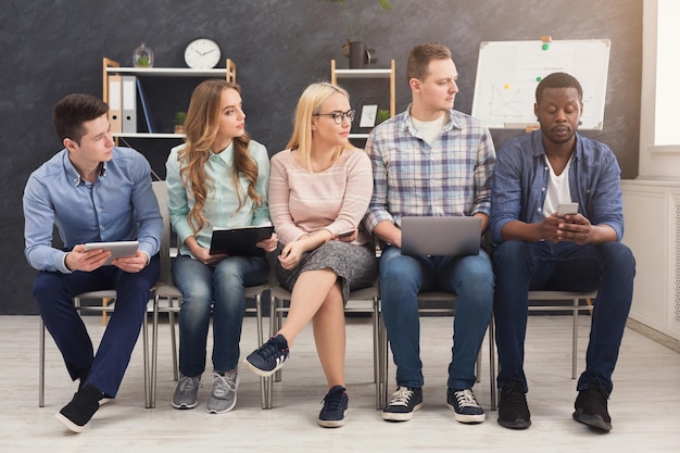 Group of business people sitting on chairs and working. Successful team using gadgets, looking at one man, communication and modern technologies concept, copy space