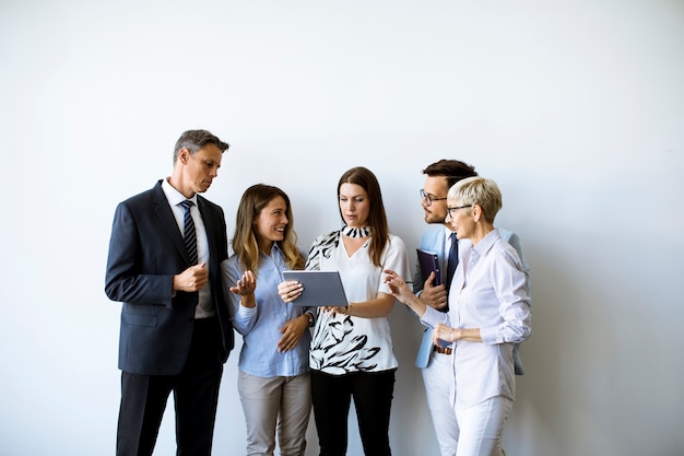 Gruppo di uomini d'affari in piedi vicino al muro e guardando la tavoletta digitale in ufficio