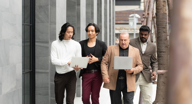 現代のオフィスビルの横にラップトップコンピュータで歩いて働くビジネスマンたちのグループ