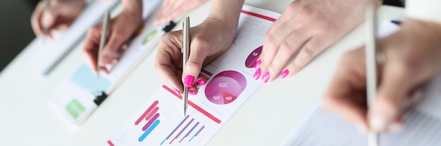 Group of business people writing with ballpoint pens in documents with graphs closeup