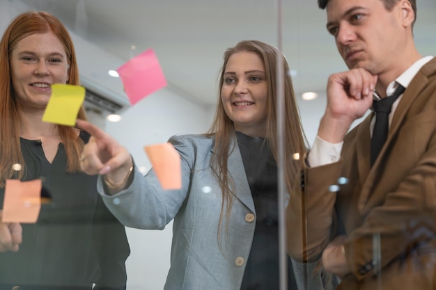 Gruppo di uomini d'affari che fanno brainstorming e scrivono idee strategiche in una nota adesiva sul vetro in ufficio