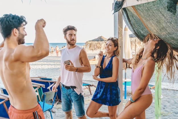 Group of carefree young people have fun talking and joking on the beach on a summer Sunday