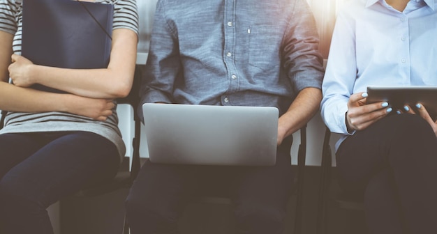 Group of casual dressed business people sitting in a line while waiting for a job interview in sunny office