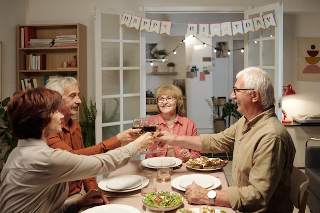 Group of cheerful aged people gathered by served festive table for dinner