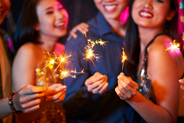 Group of cheerful friends burning bengal lights at night party when celebrating new year or birthday