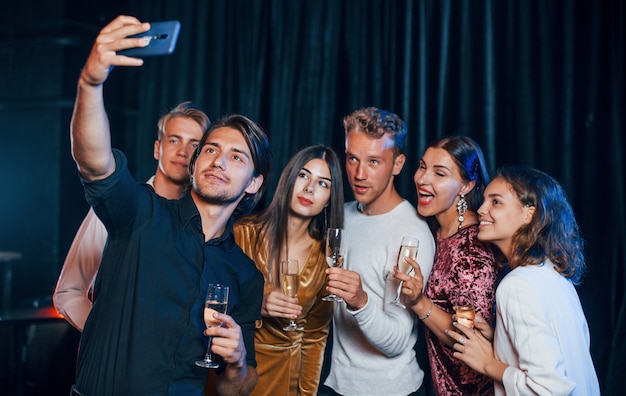 Photo group of cheerful friends celebrating new year indoors with drinks in hands.