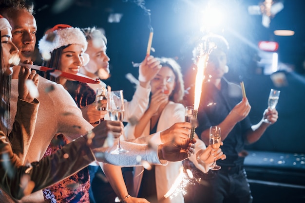 Group of cheerful friends celebrating new year indoors with drinks in hands.