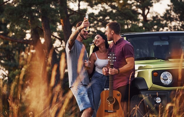 Group of cheerful friends have nice weekend at sunny day near theirs green car outdoors