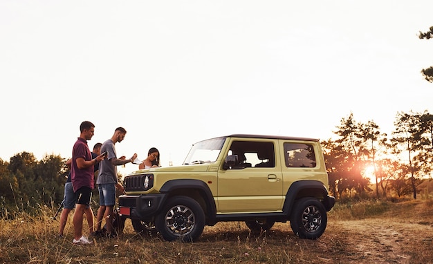 Group of cheerful friends have nice weekend at sunny day near theirs green car outdoors