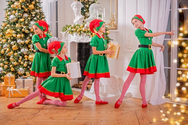 A group of cheerful happy children girls girlfriends students of a professional choreographic school in elf costumes dance with gifts against the background of a Christmas tree