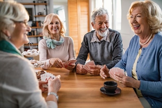 Group of cheerful mature people having fun while playing cards at home Focus is on man