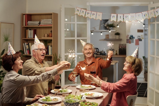 Gruppo di amici anziani allegri con luci scintillanti del bengala che festeggiano il compleanno