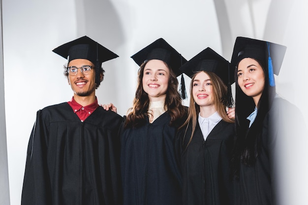 group of cheerful students in graduation caps smiling in university