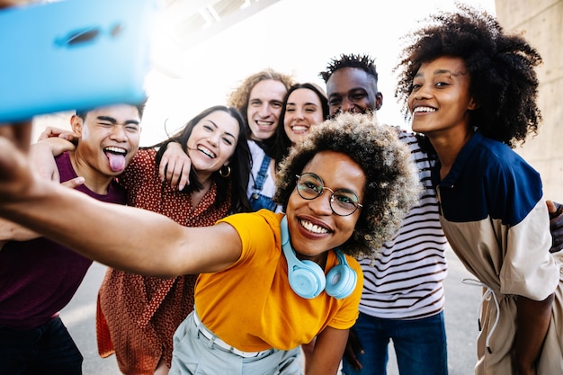 Foto gruppo di giovani allegri in abiti casual che sorridono e si fanno selfie tramite smartphone insieme