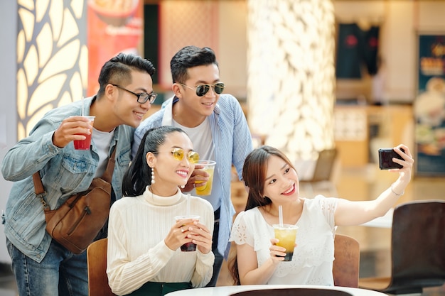 Group of cheerful young people taking selfie together with cocktaild in hands