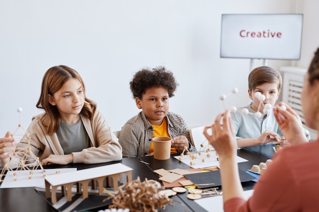 Group of children looking at female teacher demonstrating wooden models during art and craft class in school