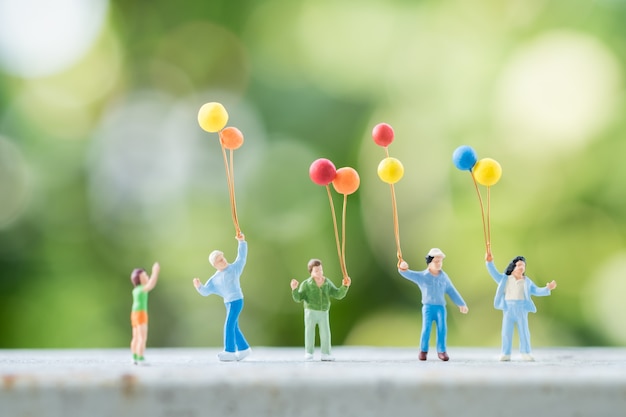 Il gruppo di figure miniatura della gente dei bambini con il pallone variopinto con la natura verde.