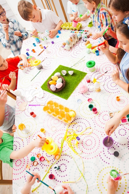 Group of children painting Easter eggs. Kids sitting at the table, top view