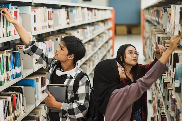 Group of college student looking for book at bookshelf, picking a book and pointing finger. Work on 