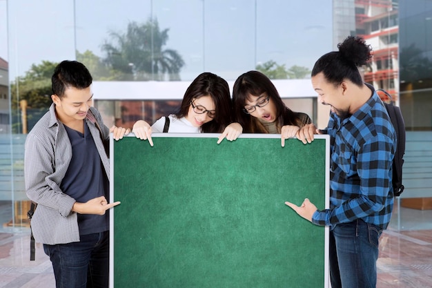 Group of college students pointing on green board with copy space