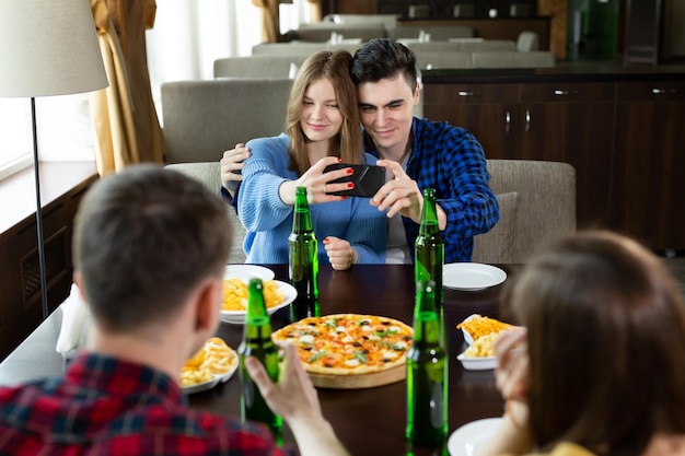 Gruppo o compagnia di giovani amici bevono birra mangiano pizza parlano e ridono e scattano selfie