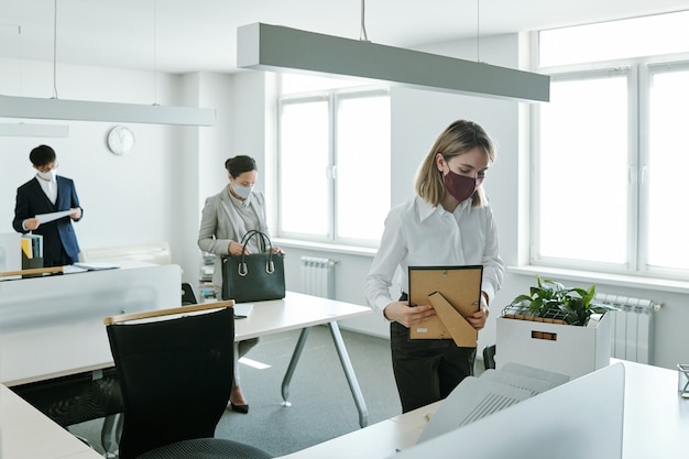 Group of contemporary business people in formalwear and protective masks taking out office supplies out of boxes before starting work