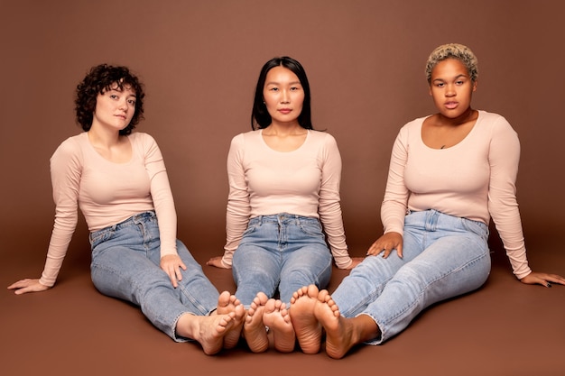 Photo group of contemporary young casual females of various ethnicities sitting on the floor with their bare feet close to each others