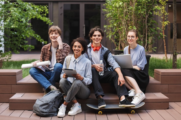 Gruppo di studenti sorridenti freddi che si siedono e felicemente